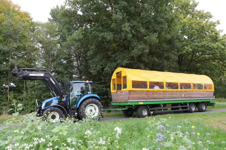 Ein Traktor zieht einen überdachten Planwagen durch die grüne Landschaft.