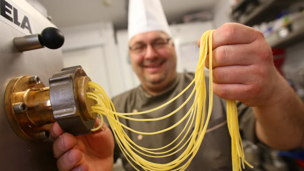 Koch hält frisch hergestellte Pasta an einer Nudelmaschine in den Händen