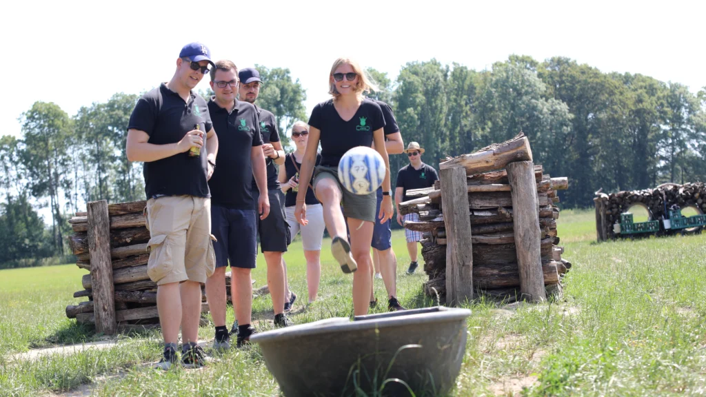 Ein Teilnehmer schießt einen Fußball über den Fußballgolf-Parcours, während die Gruppe zuschaut.